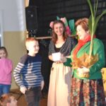 Na zdjęciu grupa dzieci stojących przed kobietą. Kobieta trzyma w rękach rośliny.