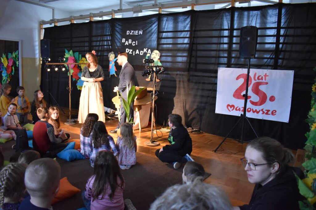 Na wolności jest grupa dzieci siedząca na scenie. W tle można wyodrębnić część sceny, która stanowi ich tło do występu.