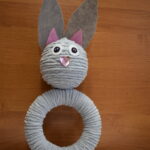 3-Miejsce-w-3-kategorii Na karcie jest robione rzemiosło kota, wykonane z zestawu owiniętego szarego włóczkiem, do którego zostały utworzone papierowe uszy i narzędzia. Tło zapewnij drewniane deski.