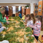 Na zdjęciach dzieci są zaangażowane w ręczne prace plastyczne, na zdjęciach są zielone dekoracje oraz inne materiały do kreatywnej zabawy. Pracami maluchów nadzoruje dorosła osoba.