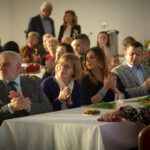 Na obrazku widać grupę ludzi siedzących przy ukradniętych i oklaskujących coś lub kogoś. Mają na twarzach rozwiązanie problemu i zadowolenia, które następuje po zakończeniu konfiguracji spotkań.