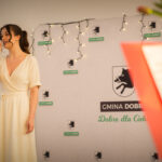 Na obraz kobiety w sukience, która śpiewa do mikrofonu. Wygląda na to, że jest w trakcie występu, zwracając uwagę na jej ekspresję i profesjonalnego sprzętu muzycznego dookoła.