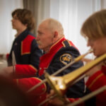 Na obrazku mężczyznę, który gra na puzonie. Wydaje się być zanurzony w swoim komputerze, z skupieniem wydobywania dźwięków ze swojego instrumentu.