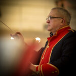 Na obrazku jest mężczyzna trzymający pałkę w dłoni. Wygląda na skupionego, być może jest dyrygentem lub atletą biorącym udział w sztafecie.