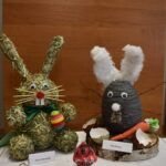 Wyroznienia-w-1-kategorii Na obrazku widoczne są dwa elementy wykonane wielkanocne króliczki utylizowane ze słomy i materiału, które są wyrzucane na drewnianą powierzchnię. Każdy z królików ma przy sobie metkę z nazwą.