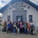 Na zdjęciu widocznym dla grupy dzieci i dorosłych stojących przed wejściem Muzeum Konstantego Laszczki pod chmurką. Wszyscy pozują do zdjęć, które są widoczne w imponującym muzeum architektonicznym.