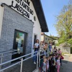 Nagranie wideo jest grupą dzieci i dorosłych, które stoi na zewnątrz wejścia do muzeum Konstantego Laszczki w słoneczny dzień. Wszyscy szczególni są narażeni na widoczność, a budynek muzeum jest dobrze oświetlony dzięki światłu słonecznemu.