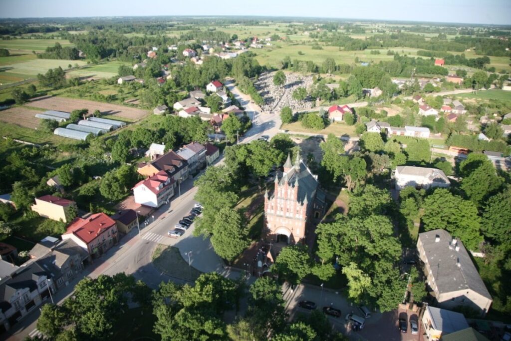 Na widocznym widoku lotniczym na małe miasteczko z widocznym ceglanym kościołem. Miasteczko otoczone jest domami, drogami i zielonymi polami.