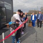 Zdj.-3 Na obrazku grupy ludzi, w tym dzieciach, biorących udział w ceremonii przecinania wstęgi przed żywym dostępem. Budynek ten nazywa się „świetlica Wólka Kokosia”.