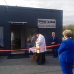 Zdj.-4 Na zdjęciu ksiądz ceremonię przecięcia wstęgi przed nowo wybudowanym wbudowanym oznaczonym jako „świetlica Wólka Kokosia”. Wokół zgromadzili się obserwatorzy, którzy wyznaczają się na uroczystość.