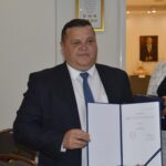 Na obrazku mężczyzn w garniturze, który trzyma otwarty segregator z dokumentami. Stał na szczeblu biurowym otoczenia.