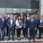 Na zdjęciu posegregowana grupa czternastu konkurencyjnych firm trzymających certyfikaty. Stoją oni na tle budynku i pozują do zdjęć.