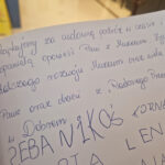 Przedstawione poniżej plan pisanej notatki w języku polskim na stronie zeszytu, wyrażającej się i dobre życzenia. W tle widoczne są kolorowe rysunki.