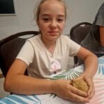 Na miejscu pojawia się młoda dziewczynka o jasnych włosach, siedząca przy stole i trzymająca w rękach kulkę ciasta. Ma sobie na sobie jasną substancję i delikatny się do aparatu.