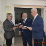 Na obrazach trzech starszych mężczyzn w garniturach wymienianych się dokumentami w dodatkowych klasycznych rzeźbach i certyfikatach na ścianach. Jeden z nich, drugiemu plakietkę, podczas gdy drugie ich z boku.