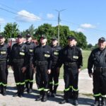 DSC_0012 Na obrazie widocznym grupy osób w mundurach, które są uwalniane w rzędzie na świeżym powietrzu pod bezchmurnym niebem. W tle znajduje się drzewo oraz kilka budynków.