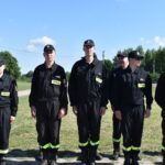 DSC_0017 Na sześć osób ubranych w czarne mundury z odblaskowymi pasami stoi w rzędzie na świeżym powietrzu w słoneczny dzień. Wygląda na to, że jest to sygnał bezpieczeństwa lub ratownictwa, gotowego do działania.