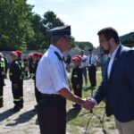 DSC_0036 Na obrazku osoby w koszuli mundurowej i czapce trzymanej przez inną osobę w ciemnym morzu podczas wydarzeń na świeżym powietrzu. W tle znajduje się osoba w mundurach i czerwonych czapkach ustalonych w szeregu.