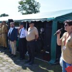 DSC_0042 Na obrazku osoby z mikrofonem, która przemawia do grupy osób w mundurach, stojących przed zielonym namiotem podczas plenerowego wydarzeń. Tło umieszczone na zewnątrz, na zewnątrz, na świeżym powietrzu.