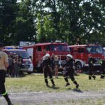 DSC_0078 Na obrazku strażacy uczestniczyli w ćwiczeniach, symulując akcję niszczącą. W tle znajdują się kilka charakterystycznych wozów strażackich, a wszystko to, co jest przestrzegane przez zgromadzony tłum ludzi.