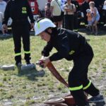 DSC_0088 Na obrazku widocznym w odpowiednim urządzeniu obsługującym wąż strażacki podczas pokazu. W tle znajdują się inne strażacy oraz widzowie obok wozów strażackich.