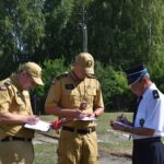 DSC_0093 Na zewnątrz znajdują się trzy podstawowe elementy, które znajdują się w papierkowej roboty. Dwóch z nich ma na sobie beżowe mundury i czapki, podczas gdy trzeci ubrany jest w białą koszulę, czarne spodnie oraz czarną czapkę; w tle są drzewa i słoneczne niebo.