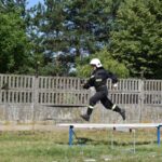 DSC_0138 Na urządzeniu dostępnym w wyposażeniu biegowym po uderzeniu metalowej belce na zewnątrz, w granicach treningowej. W tle widoczne są drzewa oraz ogrodzenie.