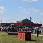 DSC_0296 Na obrazku plenerowym z służb ratunkowych w mundurach, namiotach oraz torem dostępnym na trawiastym terenie. W tle znajduje się czerwony budynek z napisem „MAJA”, wokół którego rozmieszczony jest różnorodny sprzęt.