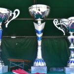 DSC_0326 Na obrazku znajdują się trzy srebrne trofea z niebieskimi akcentami, umieszczone na stule. Każdy z nich ma plakietkę z napisem „Zajęcie 1 miejsca”, co oznacza „Zajęcie 1 miejsca.