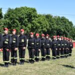 DSC_0334 Na obrazku widać grupę umundurowanych osób w czapkach, stojących w szeregu na trawiastej powierzchni. W tle znajduje się drzewo, a przed osobą o dostępie do informacji.