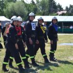DSC_0342 Na obrazku znajduje się grupa pięciu osobników w czarnych mundurach i hełmach, stojących w formacji, z charakterystycznymi emblematami na kamizelkach. W tle widoczni są widzowie, w tym dzieci, które zwracają uwagę na zewnątrz.