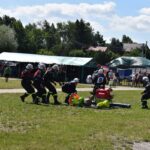 DSC_0344 Na zewnątrz znajduje się zespół, który jest w mundurach, który ma udział w działaniach na zewnątrz, obsługując sprzęt na trawiastym terenie. W tle są namioty oraz widoczny się widzowie.