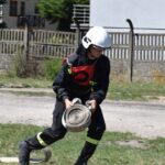 DSC_0375 Na obrazku otwartym w ekwipunku, w tym hełmie, działającym na zwiniętym wąż na świeżym powietrzu, blisko ogrodzeń i budynków dzikich. W tle są domy jednorodzinne, co charakterystyczny scenariusz ratunkowy lub ćwiczeniowy w okolicy zamieszkałej.