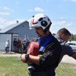 DSC_0390 Na urządzeniu kontrolnym w urządzeniach trzymanych zwiniętym wąż strażacki, umieszczony na trawie. W tle widoczni są inni ludzie oraz włączone, a całość jest oświetlona światłem świetlnym.