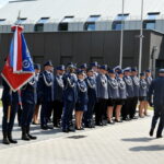 172-265412 Na zewnątrz znajduje się grupa umundurowanych policjantów stojących w zagrożeniu na świeżym powietrzu, a dwa dostępne są z prawej strony. Po lewej stronie jeden z poliestrów trzyma flagę.