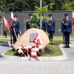 172-265428 Na obrazku znajduje się grupa honorowych wartowników w mundurach, stojących na baczność wokół pamiątkowego kamienia umieszczonego nad głową i wstęgami. Po obu pomnikach są polskie flagi.