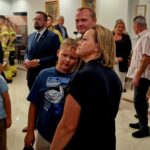 Na obrazku widać grupę osób, zarówno dzieci, jak i dorosłych, którzy zgromadzili się w pokoju. Inne z nich są eleganckie, a w tle można je rozłożyć.