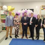 Na obrazku znajduje się sześć osób stojących w pokoju udekorowanym łukiem z balonów oraz złotymi serpentynami, świętującymi 5. rocznicę. członkowie byli na szczęśliwych i świadomych w życiu.