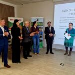 Na obrazie pojawia się grupa ludzi, która jest przedstawiona przed prezentacją prezentacyjną, która jest wyświetlana jako slajd w języku polskim. Wskazuje na, że uczestniczyą w sesji szkoleniowej.