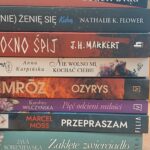 Na stosie znajduje się kilka książek, które są zawarte w języku polskim, a na grzbietach znajdujących się w tytułach i autorze publikacji. Książki są przedmiotem zainteresowania czytelników.