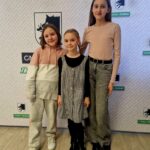 484297046_675894741452717_1709509082578748964_n Na obrazku troje dzieci stoi przed tłem z logo i napisami, uśmiechając się do kamer. Dzieci wyglądają na zadowolone i są przeznaczone do walki z atakiem promocyjnym.