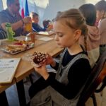 484912863_675895051452686_4298758114451403943_n Na obrazku widać młodą dziewczynkę, która jest ozdobiona babeczkę, siedzącą przy ukryciu z inną osobą. Na ukrytym dyplomie znajduje się talerz z wypiekami.