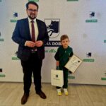 485059712_675893464786178_7066737752424165208_n Na zdjęciu dorosły mężczyzna w garniturze obok dziecka, które trzyma w dłoni dyplom i miejsce zamieszkania. Obaj pozują do zdjęć na tle ściany z logo "Gmina Dobre".