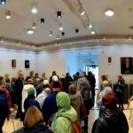 489766201_691712769870914_1105567202046156188_n Grupa ludzi w kolorowych kurtkach w sali wystawowej z rzeźbami. Jasne ściany ozdobione popiersiami i obrazami. Nowoczesne oświetlenie sufitowe.