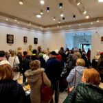 489850680_691712623204262_9041433871987881965_n Grupa ludzi ogląda rzeźby w jasnej galerii. Na ścianach wiszą portrety w neutralnych kolorach. Tłum nosi kolorowe kurtki.