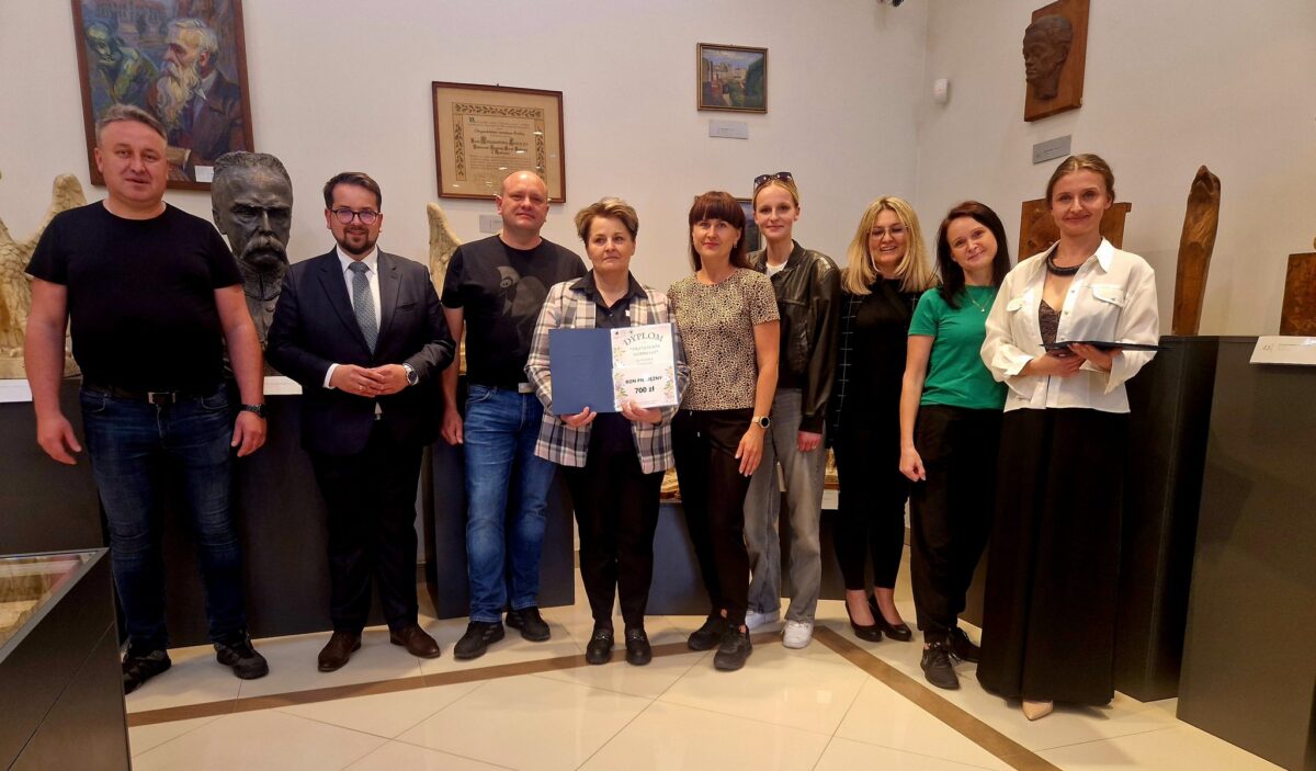 Na obrazku grupa ośmiu osób stoi w muzeum. Tło zdobią rzeźby i obrazy w neutralnych kolorach. Centralna osoba trzyma dyplom.