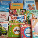 1000001226 Na zdjęciu znajduje się stos kolorowych książek dla dzieci na drewnianym tle. Okładki mają żywe kolory i różnorodne ilustracje. Każda książka przedstawia różne tematy i postacie.