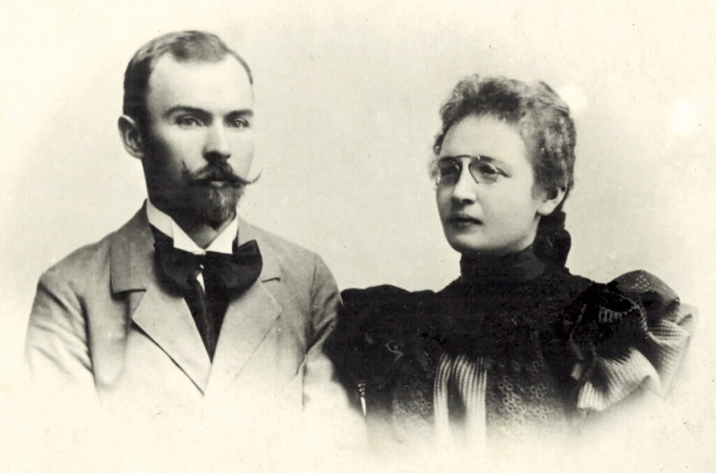 Czarno-białe zdjęcie portretowe przedstawia mężczyznę w garniturze i kobietę w okularach. Mają poważne wyrazy twarzy. Tło jasne, jednolite.