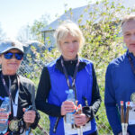 Na zdjęciu troje ludzi z medalami, ubranych w niebieskie wierzchnie. W tle ogrodzenie i zieleń. Każda osoba trzyma butelkę wody.