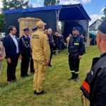 500943609_728989759476548_225227761018960032_n Grupa ludzi w uniformach stoi na trawie. W tle namiot i stóg siana. Jasny dzień, zielone drzewa w oddali.